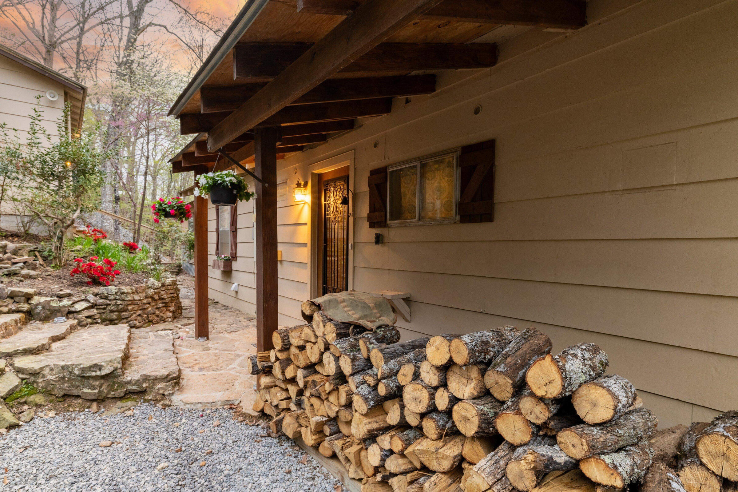 Welcome to The Lake Escape A warm and inviting entrance surrounded by native stone, flowers, and a ready-to-burn woodpile sets the tone for a peaceful, rustic getaway.